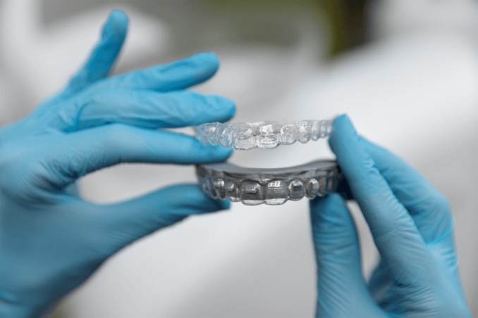 Gloved hands holding a pair of clear, removable orthodontic aligners, demonstrating the discreet technology used in an Invisalign treatment.