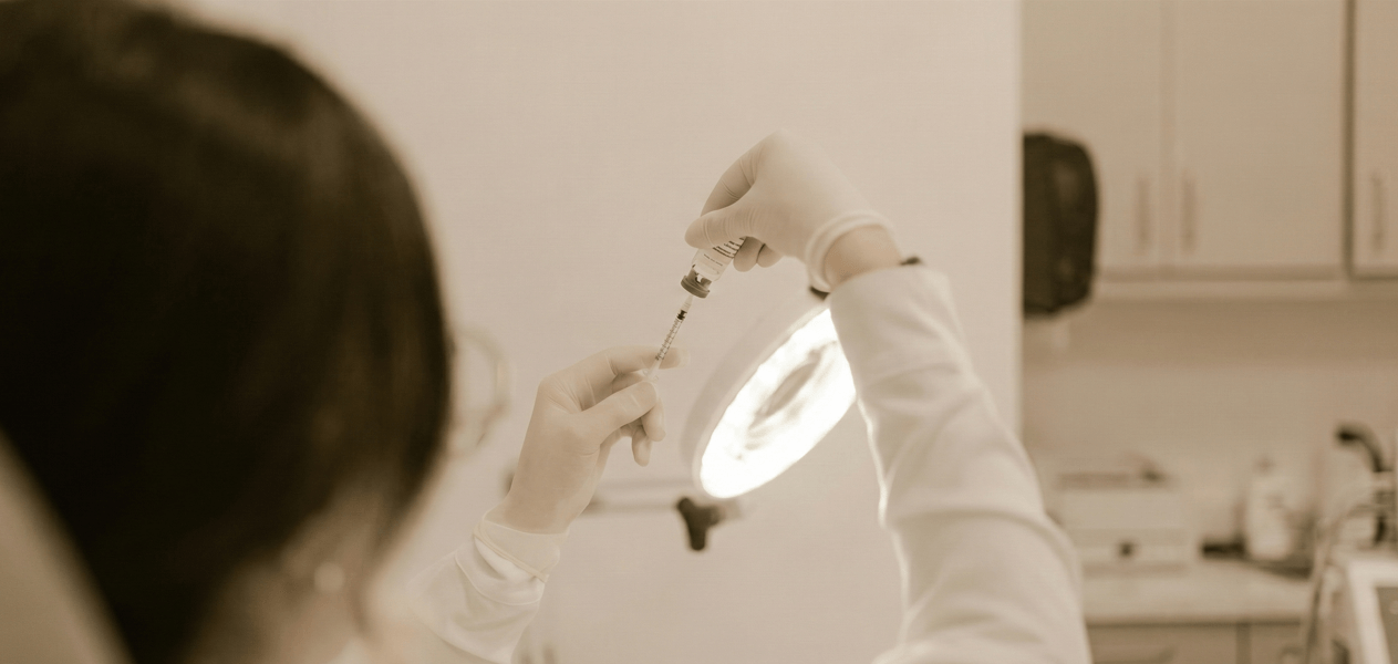 A healthcare specialist in a sterile environment prepares a syringe under a bright medical lamp, representing the precision required for a Stem-Cell Therapy treatment.